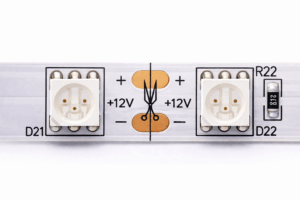 Nahaufnahme eines 12V LED-Streifens mit markierter Schnittstelle: Darstellung der kupferfarbenen Kontaktpads, Polaritätskennzeichnung (Plus und Minus) und des Scherensymbols für den exakten Trennungspunkt.